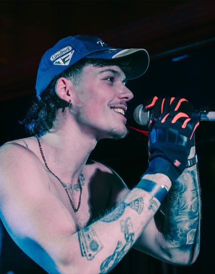 Flexx Carter performing in a blue cap, microphone in a gloved hand
